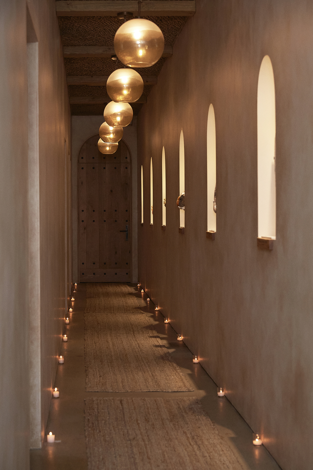The PALOMA crystal hallway — globe pendant lights, candles lining the floor, arched wooden door at the end