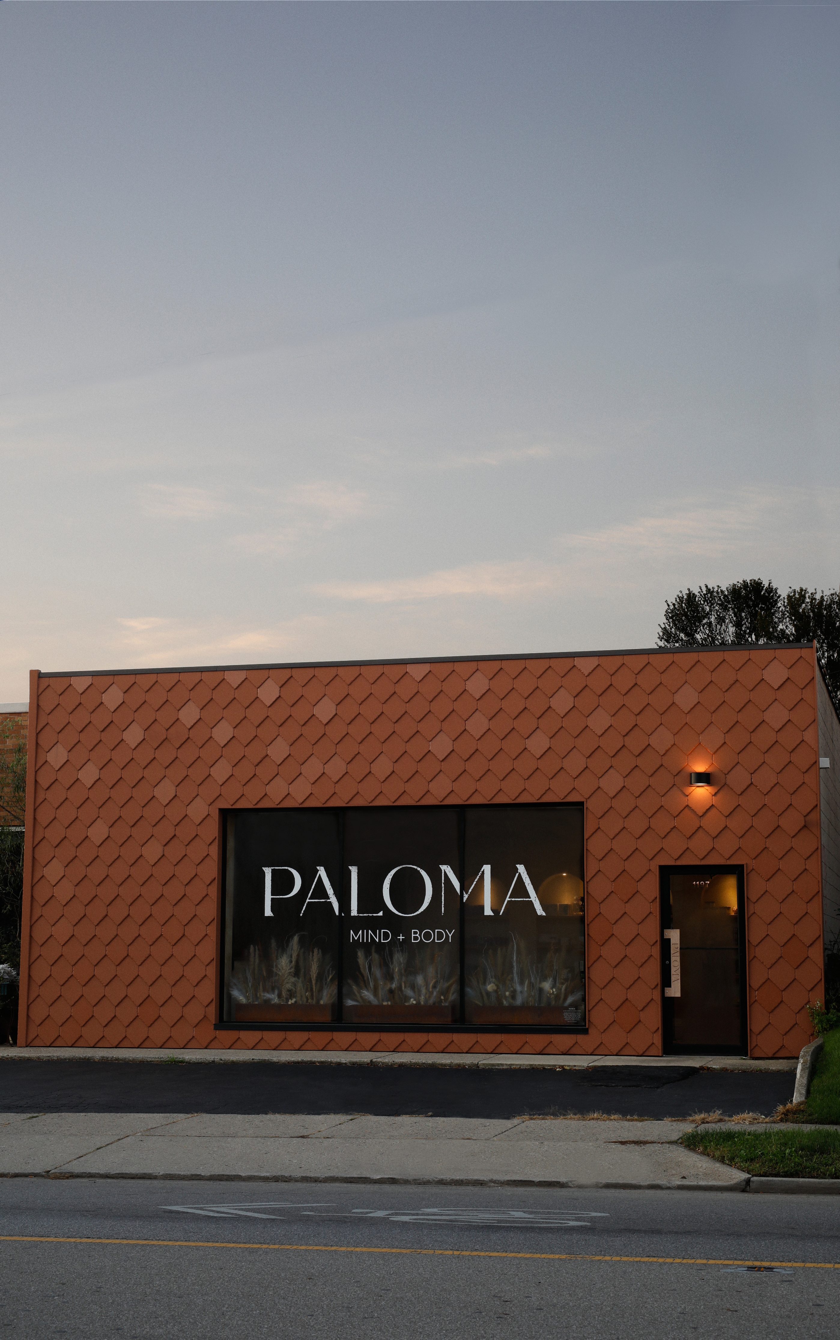 PALOMA exterior at dusk — terracotta shingle facade and illuminated storefront on W 5th Ave