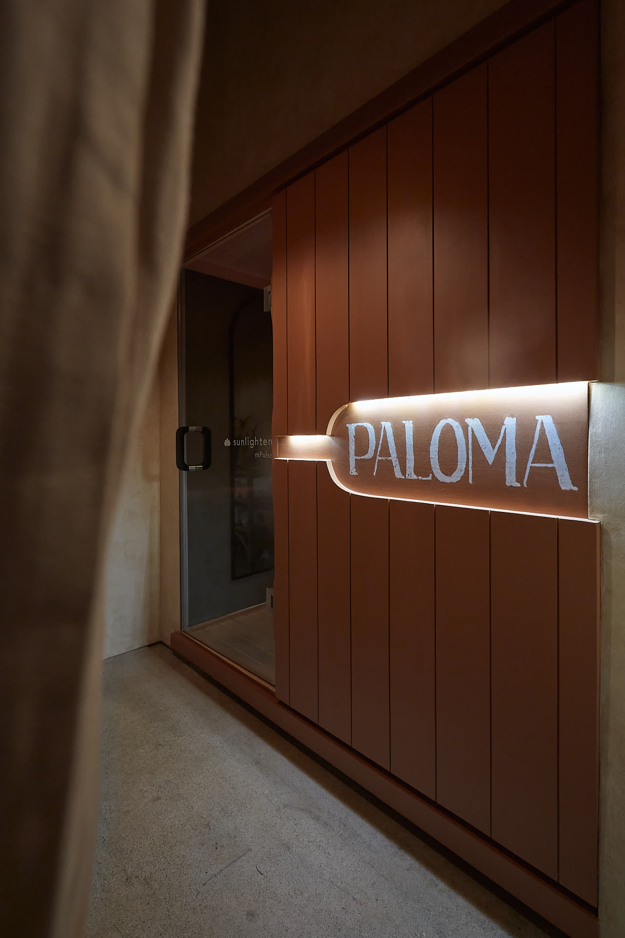 The illuminated PALOMA sign beside the sauna door, in warm timber.