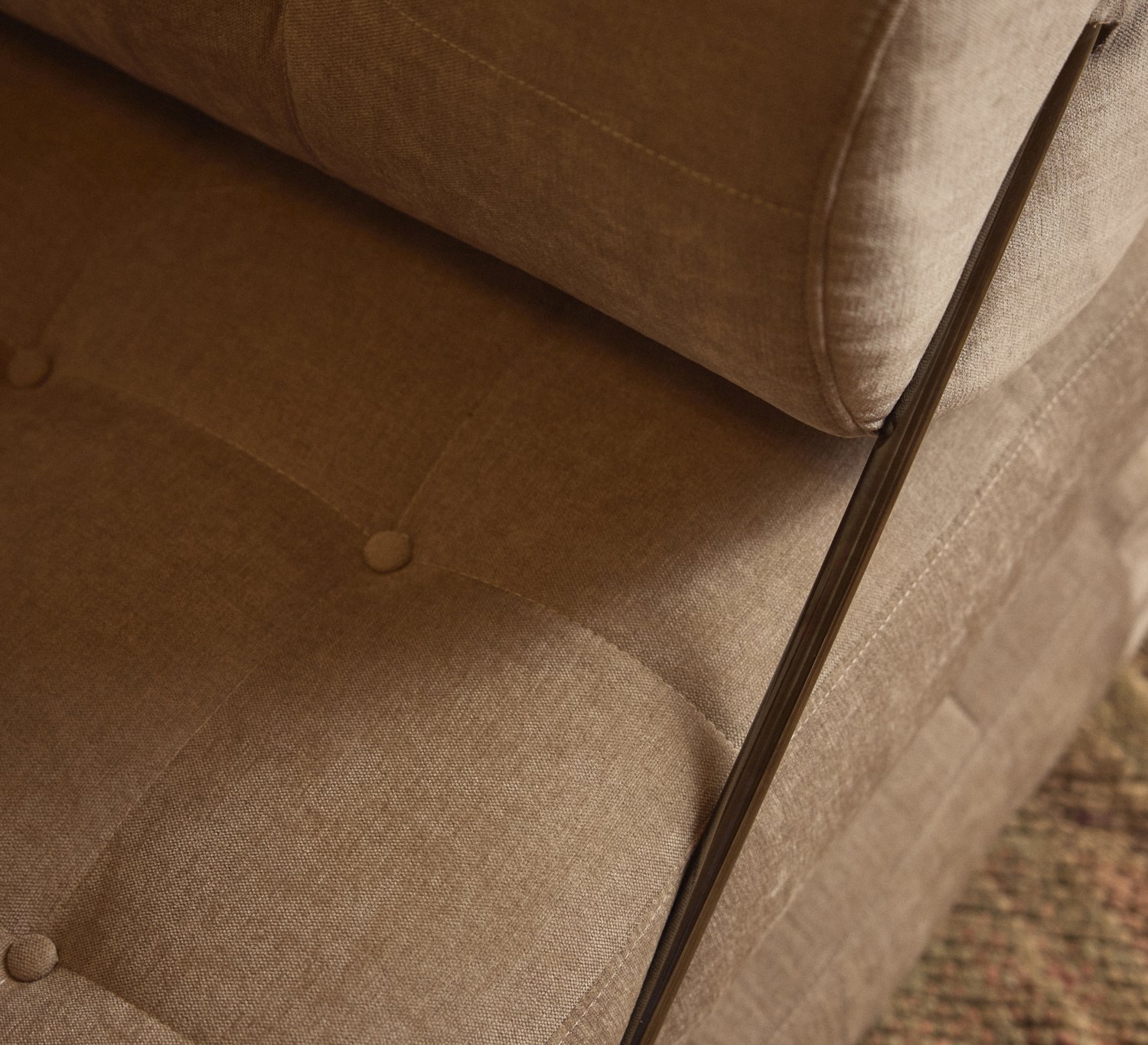 A close view of linen seating — a buttoned seam, a bolster, the woven floor beneath.